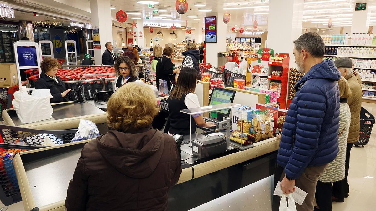 Gente de compras en un supermercado con la cajera atendiendo a clientes.