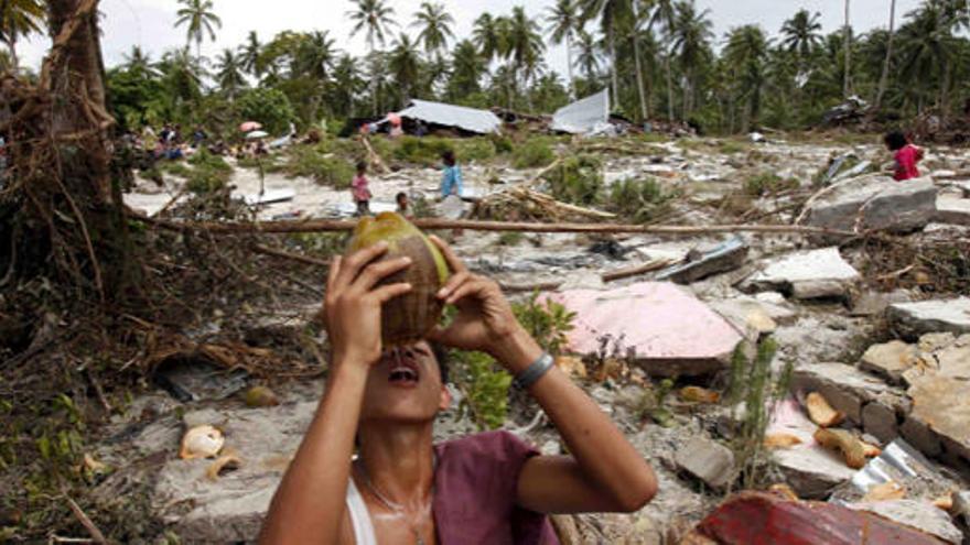 Un joven bebe agua entre los restos de una aldea devastada.