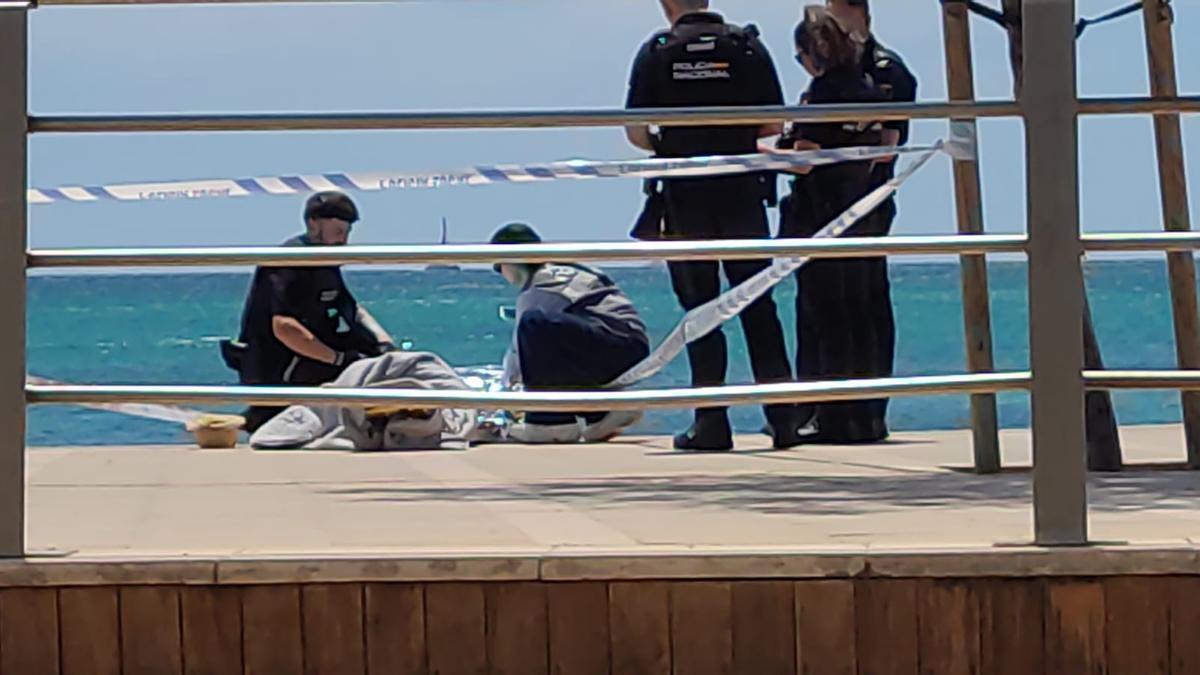 La forense examina el cadáver del hombre en el Paseo de El Molinar asistida por un agente de la Policía Nacional.