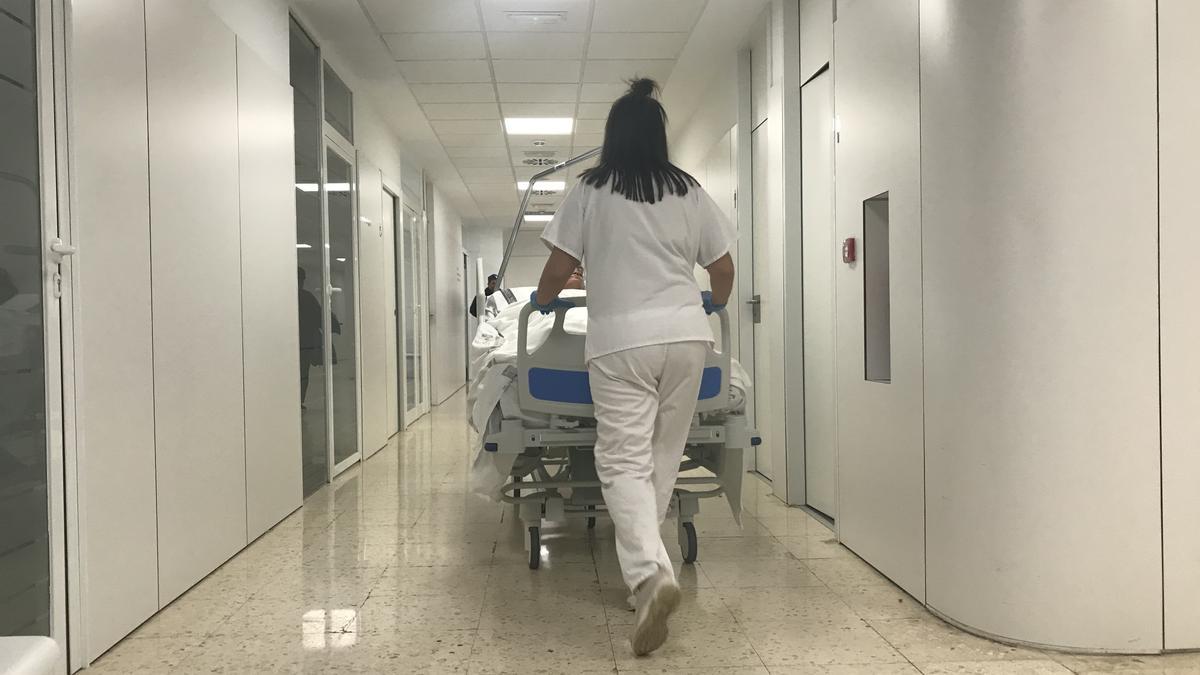 Una celadora trasladando a un paciente a planta en el Hospital General Universitario de Elda.