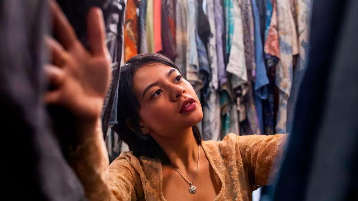 Una mujer mira entre los percheros de una tienda de ropa.