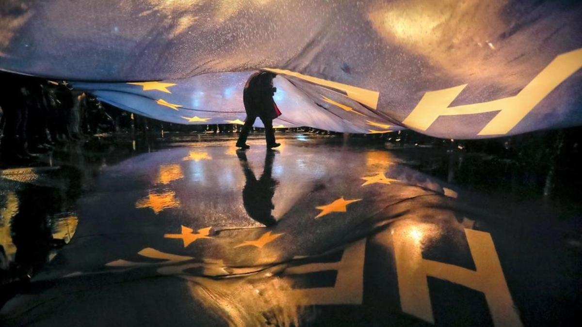 Un manifestante camina bajo una gran bandera de la Unión Europea durante una protesta frente al Parlamento rumano contra las políticas del Gobierno del país.