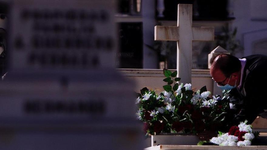 Un hombre deposita flores sobre la lápida de un difunto.