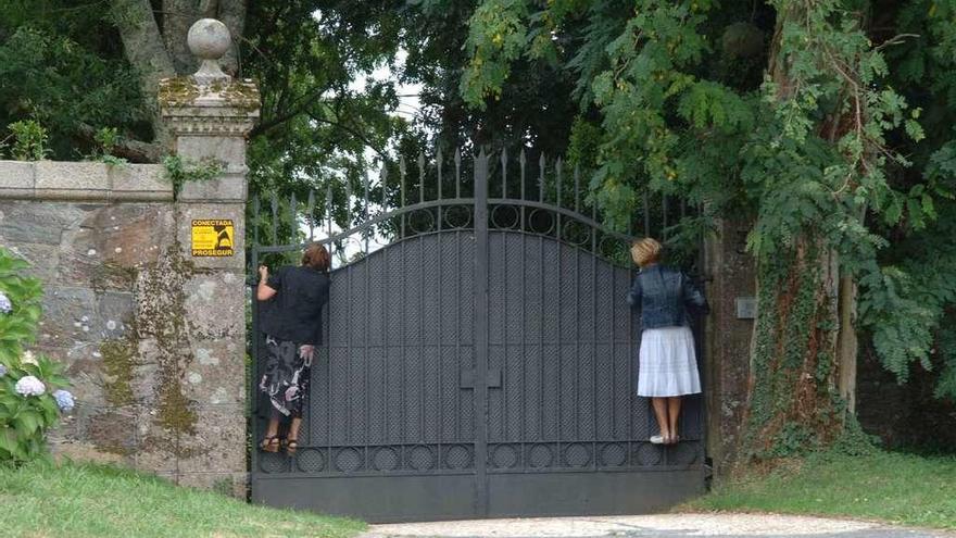 Dos mujeres intentan ver el interior de la finca del pazo de Meirás desde el portalón.