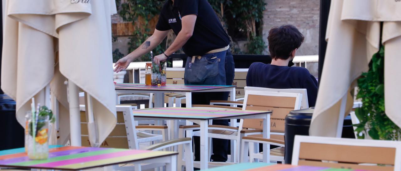 Un joven camarero recoge una mesa en una terraza de un bar de València.