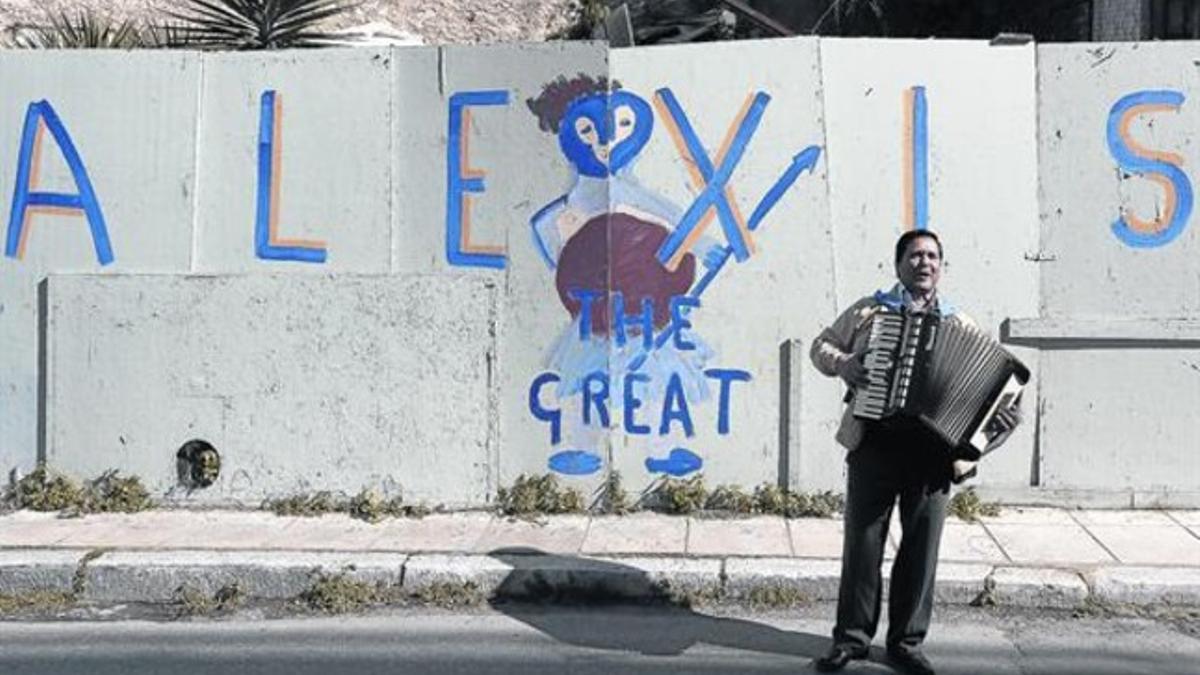 Un músico callejero en Atenas, frente a un grafiti de apoyo a Tsipras, ayer.