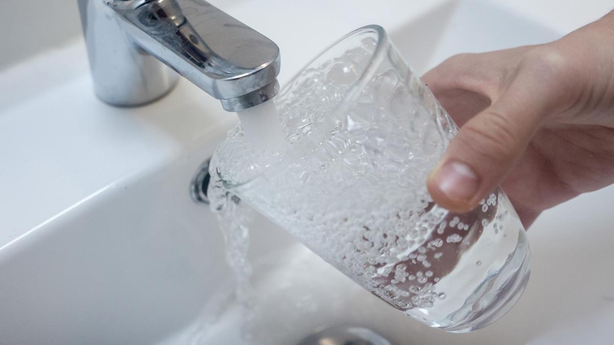 Una persona llena un vaso de agua de un grifo