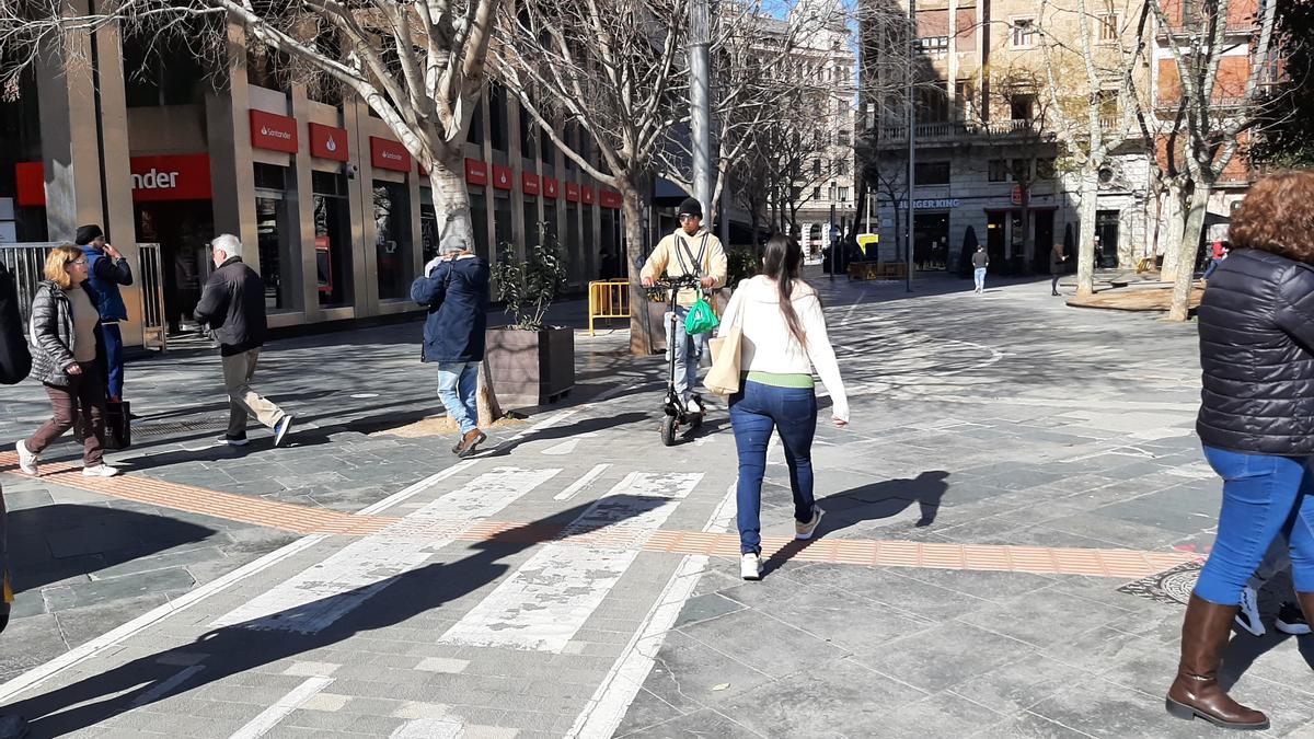 Un usuario de patinete circula por la plaza de España sorteando obras y peatones.