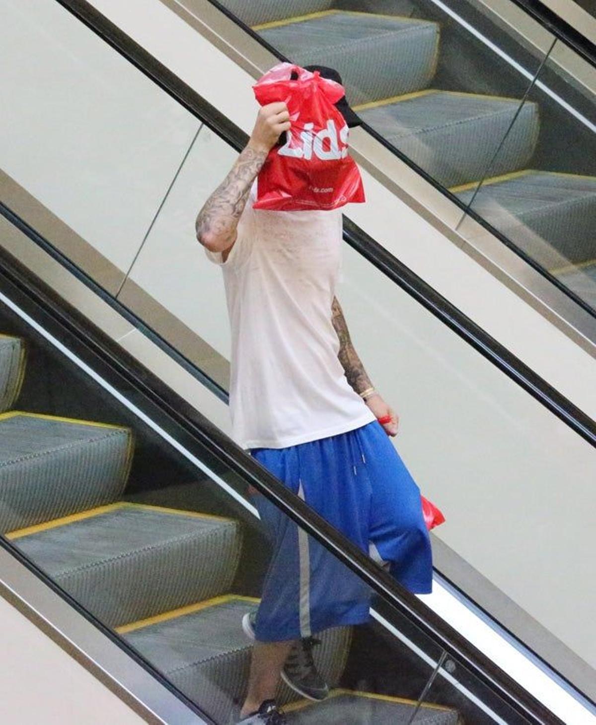 Justin Bieber se tapa con la bolsa la cara mientras baja por las escaleras mecánicas