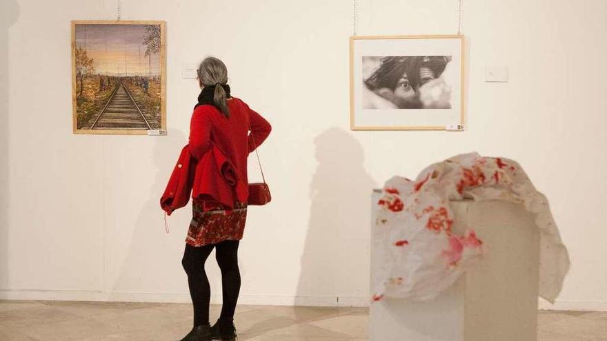 Al fondo, una mujer observa una de las pinturas de la muestra. A la derecha, ropa ensangrentada.