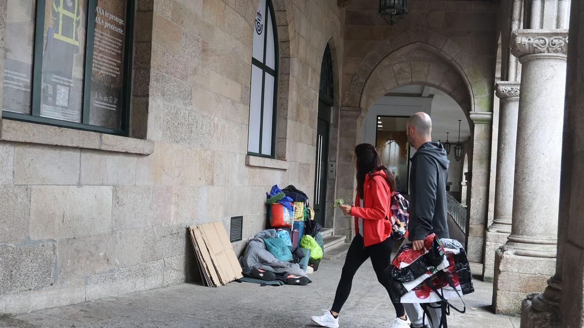 Dos viandantes junto a las pertenencias de las personas sin hogar que se asientan en los soportales de las oficinas de Correos.