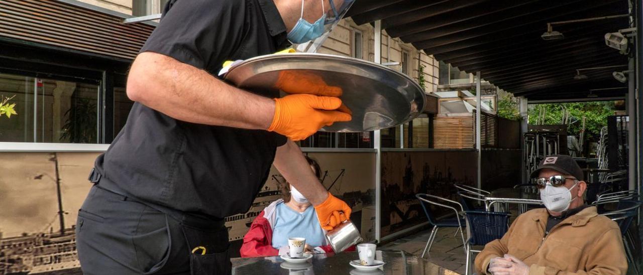 Un camarero sirve a dos clientes en una terraza.