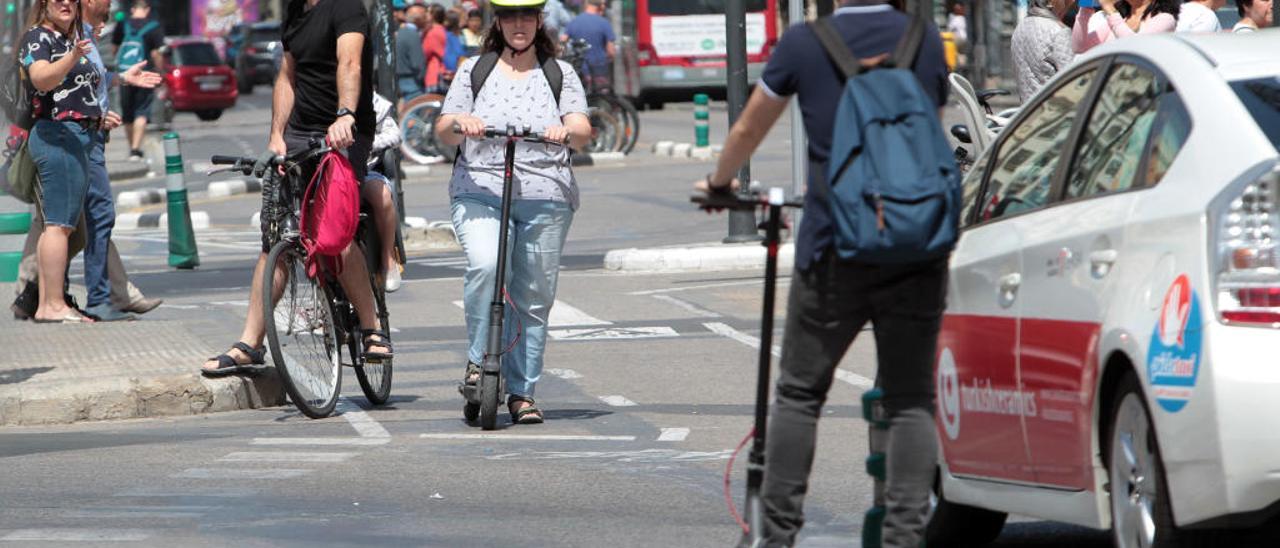 Una mujer en la calle Xàtiva circula con casco en su patinete, y otro usuario frente a ella sin casco con el mismo modelo.