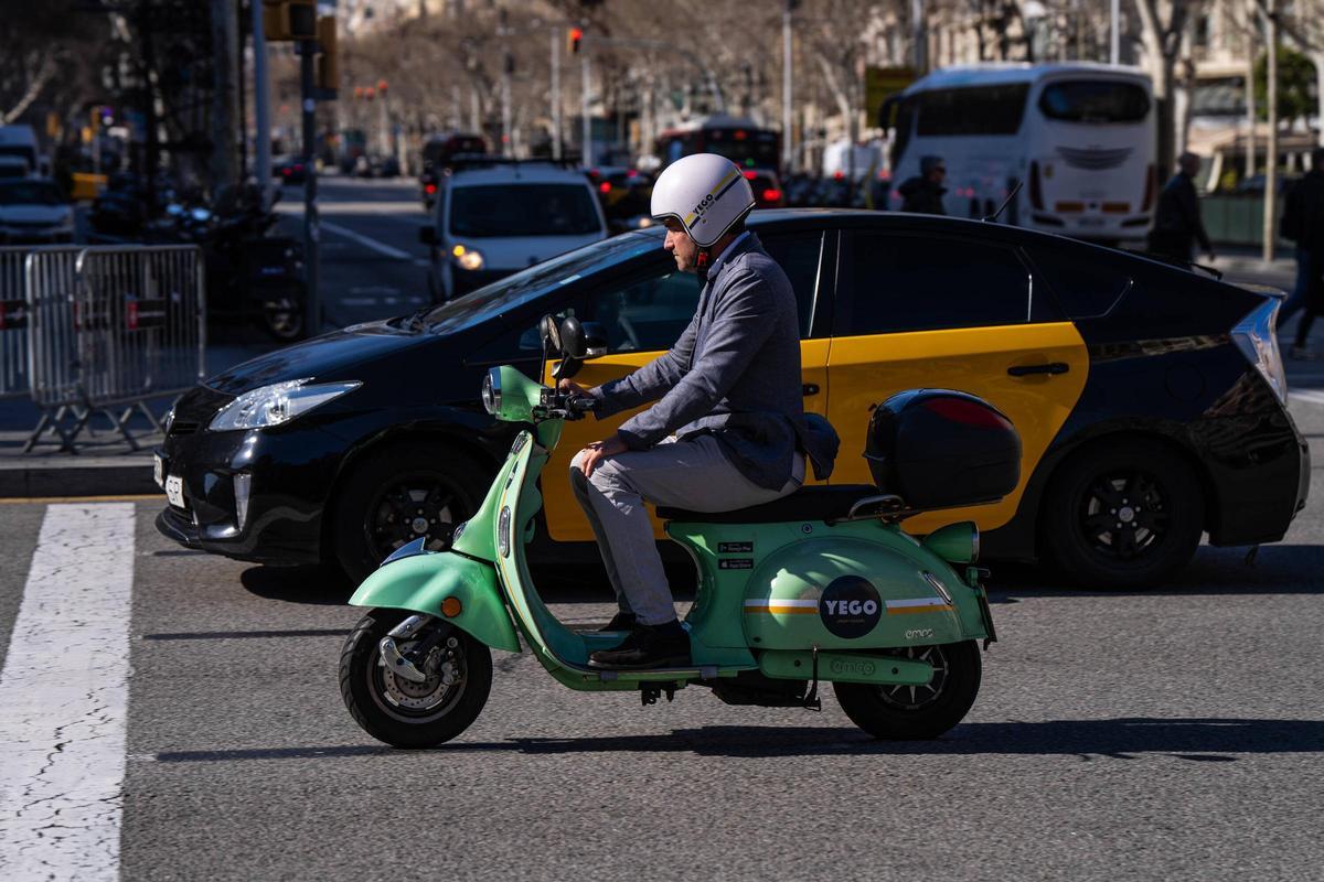 Una moto de Yego, junto a un taxi, circula por el paseo de Gràcia, este martes