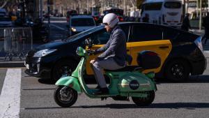 Una moto de Yego, junto a un taxi, circula por el paseo de Gràcia, este martes