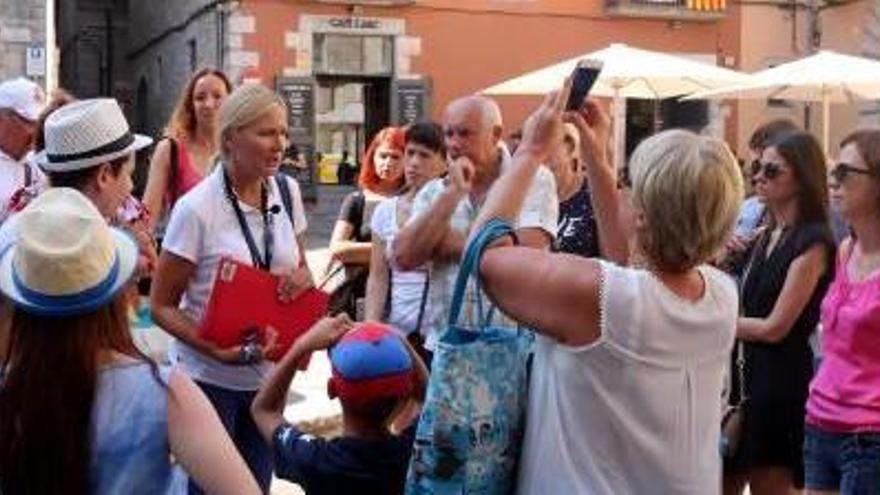 Un grup de turistes amb la seva guia, que porta penjat al coll un micròfon, i turistes caminant pel carrer de la Força de Girona.