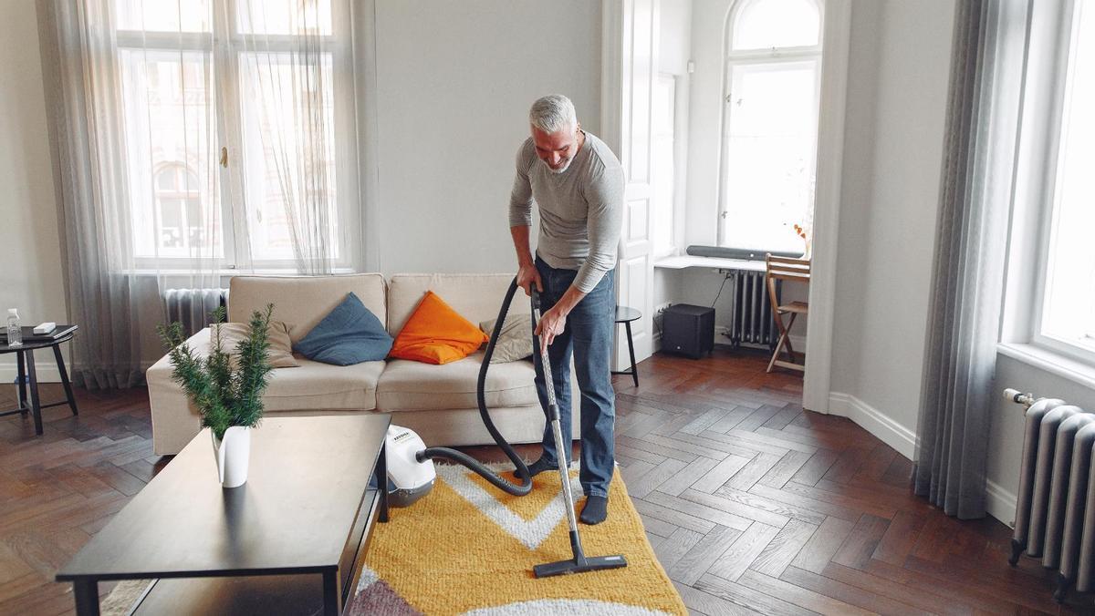 Un hombre limpia la alfombra de su vivienda.