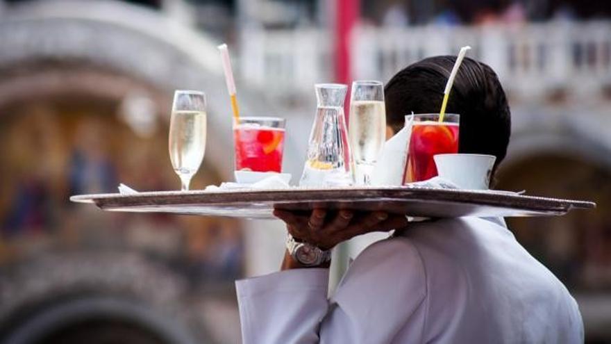 Un camarero lleva una bandeja con bebidas.