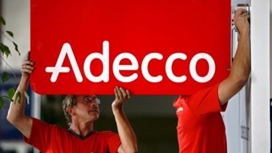 Unos trabajadores instalan un cartel de la empresa de trabajo temporal suiza, Adecco.
