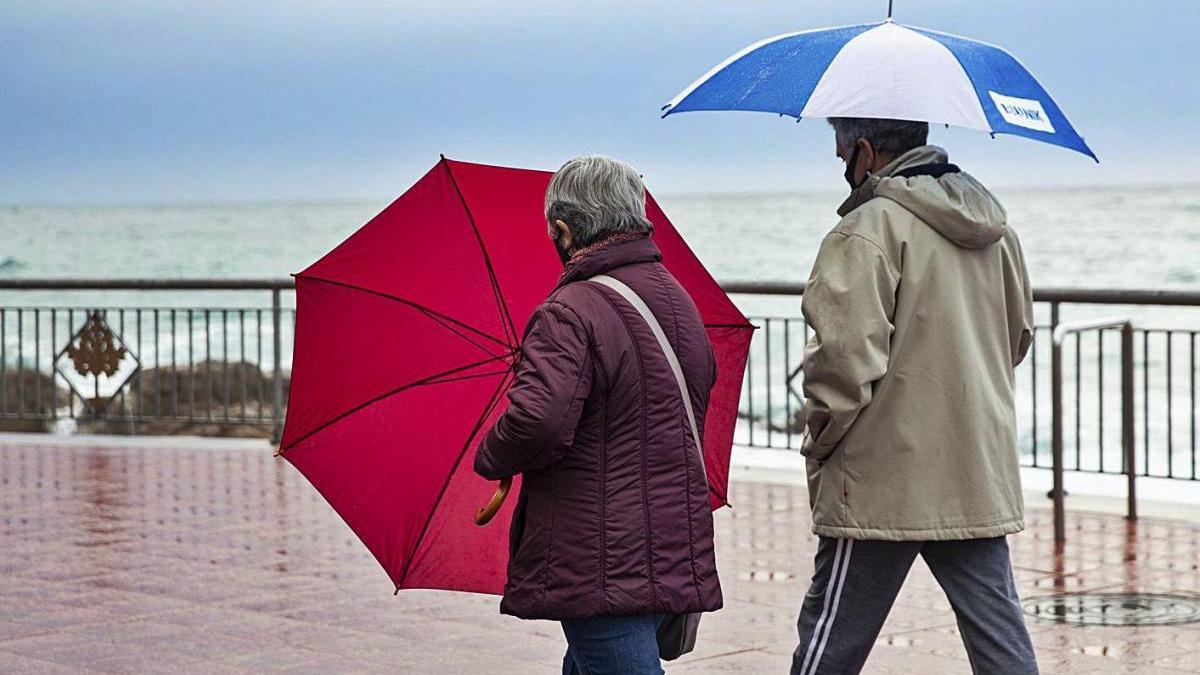 Gent passejant ahir per Blanes sota la pluja i amb el temporal marítim de fons.