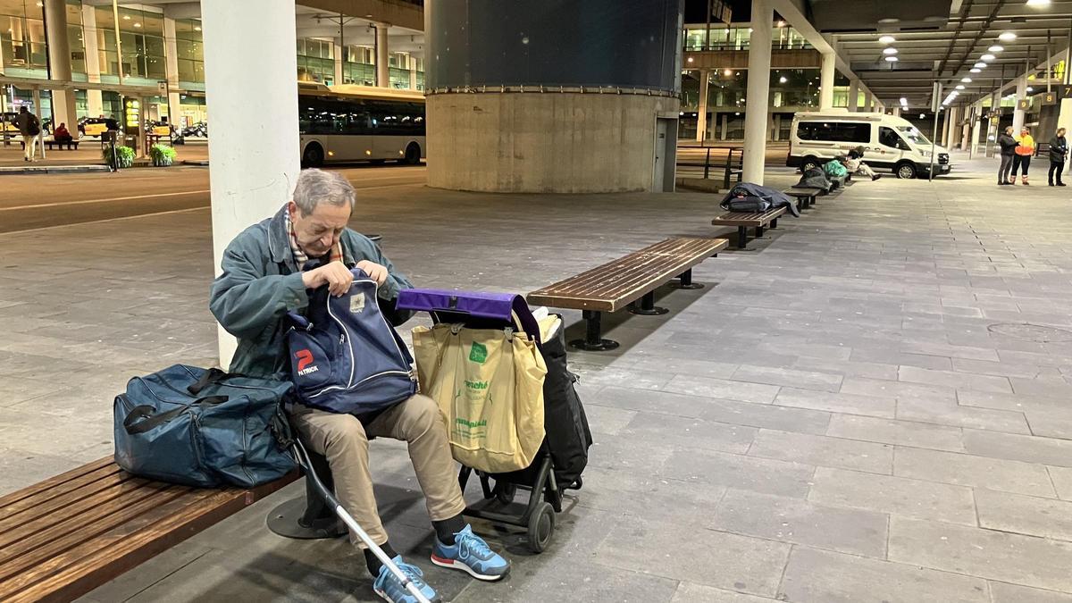 Dominico, un hombre sin hogar, busca las pastillas para la presión tras ser desalojado de la terminal T1, mientras otros sintecho duermen en los bancos.