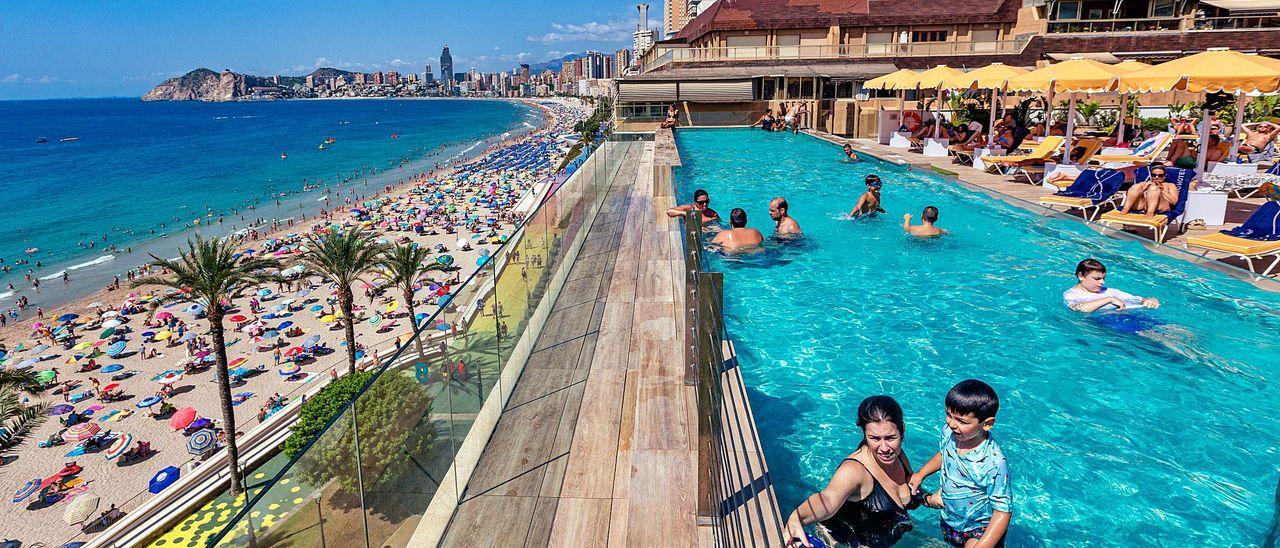 Turistas toman un baño en la piscina de un hotel de Benidorm ubicado frente a la playa de Poniente, también llena de bañistas esta misma semana.