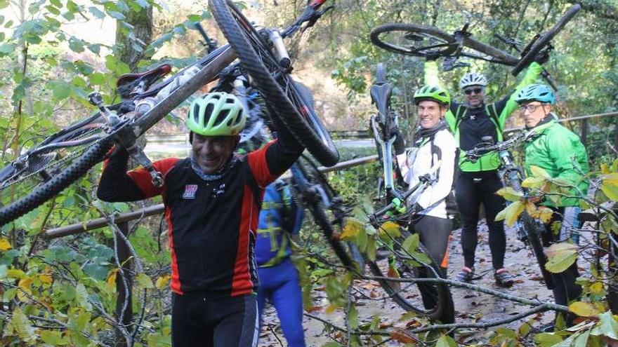 Un grupo de ciclistas en la Senda del Oso con las bicicletas sobre la cabeza para sortear los árboles caídos.