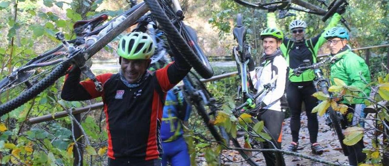 Un grupo de ciclistas en la Senda del Oso con las bicicletas sobre la cabeza para sortear los árboles caídos.