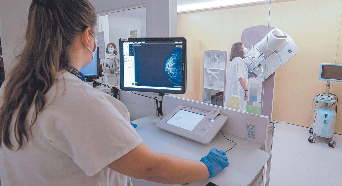 Una profesional sanitaria realiza una mamografía a una paciente en una sala de exploración.