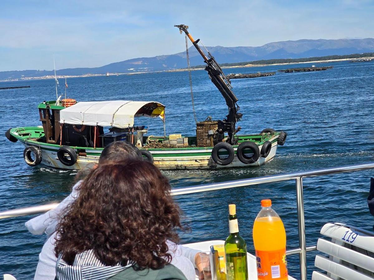 Los viajeros de un catamarán observan un barco que traslada ostra.