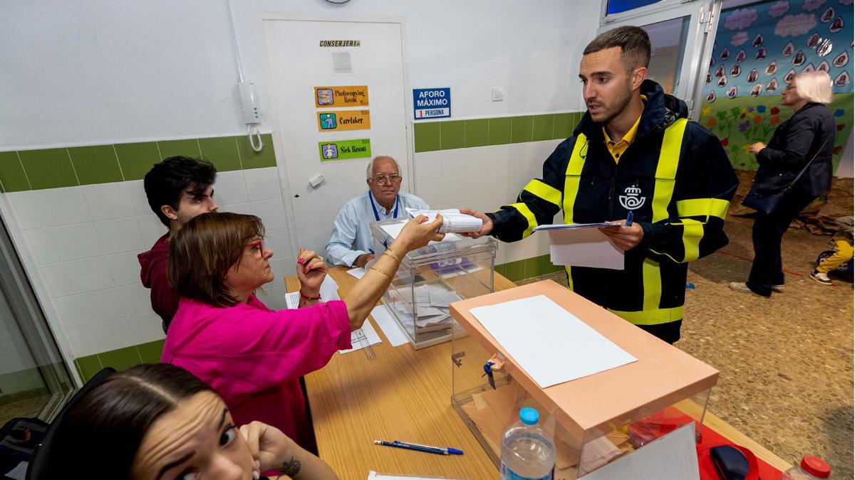 Un cartero entrega a la presidenta de una mesa electoral el voto por correo que corresponde a esa mesa, en el colegio de San José de Lorca.