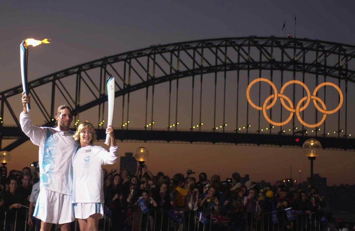 El tenista australiano Patrick Rafter y la actriz y cantante Olivia Newton John, tambien australiana, hacen el relevo de la antorcha con la LLama Olímpica, con el Harbour Bridge al fondo, esta tarde. Los Juegos Olímpicos de Sydney 2000 darán comienzo mañana, día 15