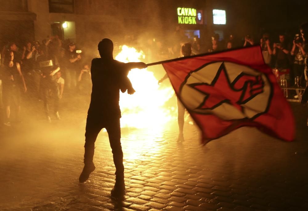 Un manifestante agita una bandera delante de la basura ardiendo durante la manifestación contra el G-20 en Hamburgo, Alemania