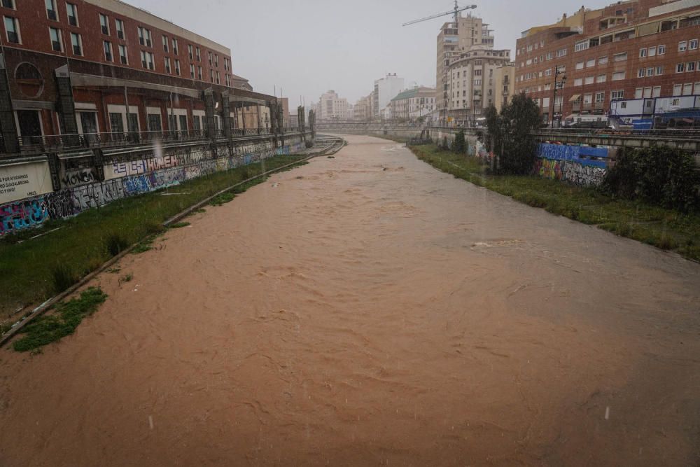 El río Guadalmedina crecido con agua y calles del Centro y el entorno del cauce, desiertas bajo la lluvia, la estampa de este martes 31 de marzo.