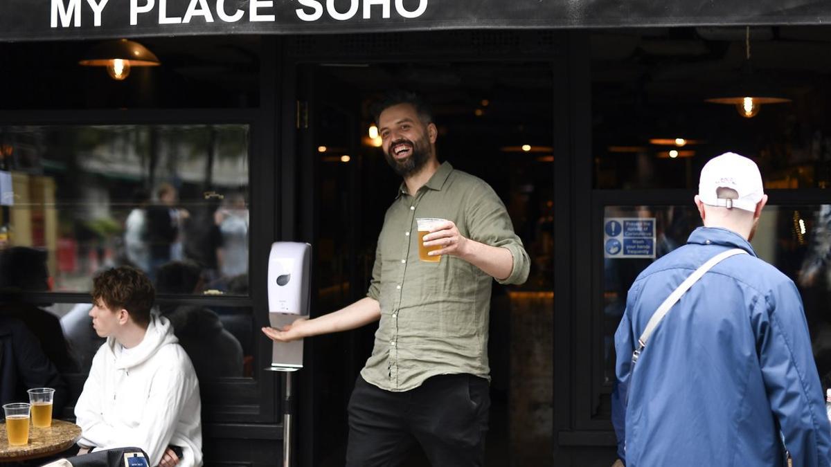 Un hombre sale con una cerveza en la mano de un pub en Londres.