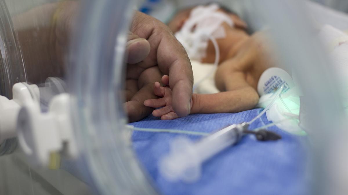 Un padre coge la mano de su hijo prematuro en el hospital.
