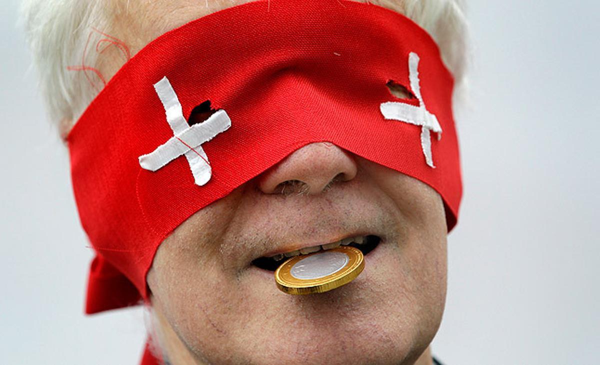 Un home es tapa els ulls amb una banda que simula la bandera de Suïssa, en una manifestació a Berlín contra un acord fiscal per evitar l’evasió d’impostos assolit entre Suïssa i Alemanya.