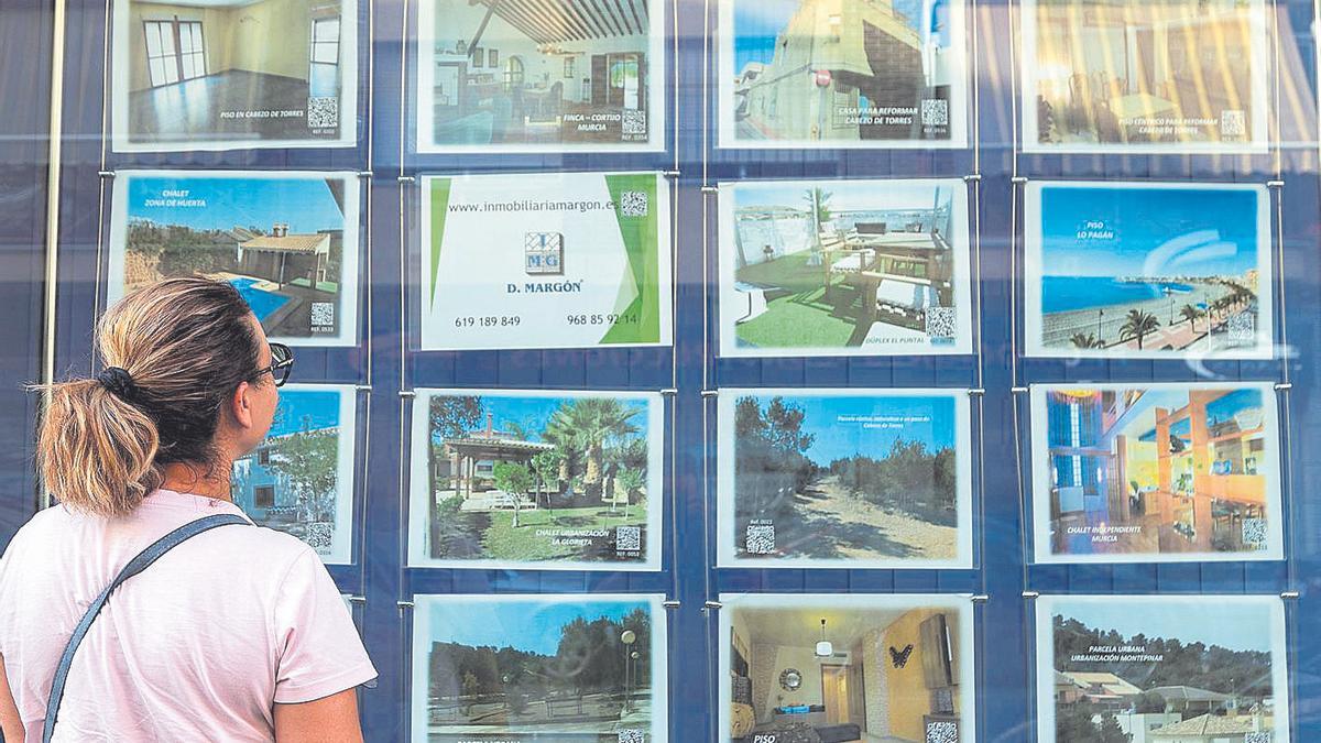 Una mujer mira carteles en los que se anuncian viviendas en venta en una inmobiliaria de Murcia.