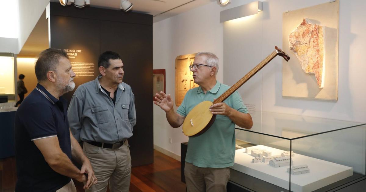 Por la izquierda, Manuel Paz, Chus Puras y Carlos González, con la réplica de la cítara de Lillo, en el Museo Arqueológico, junto a una recreación de la pintura del músico a sus espaldas. | fernando rodríguez