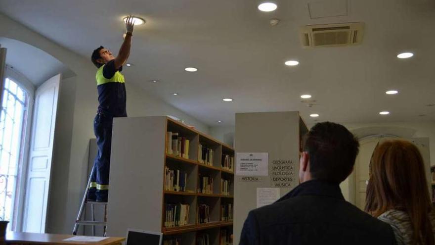 Un electricista colocando una de las luces bajo la mirada del alcalde y la bibliotecaria.