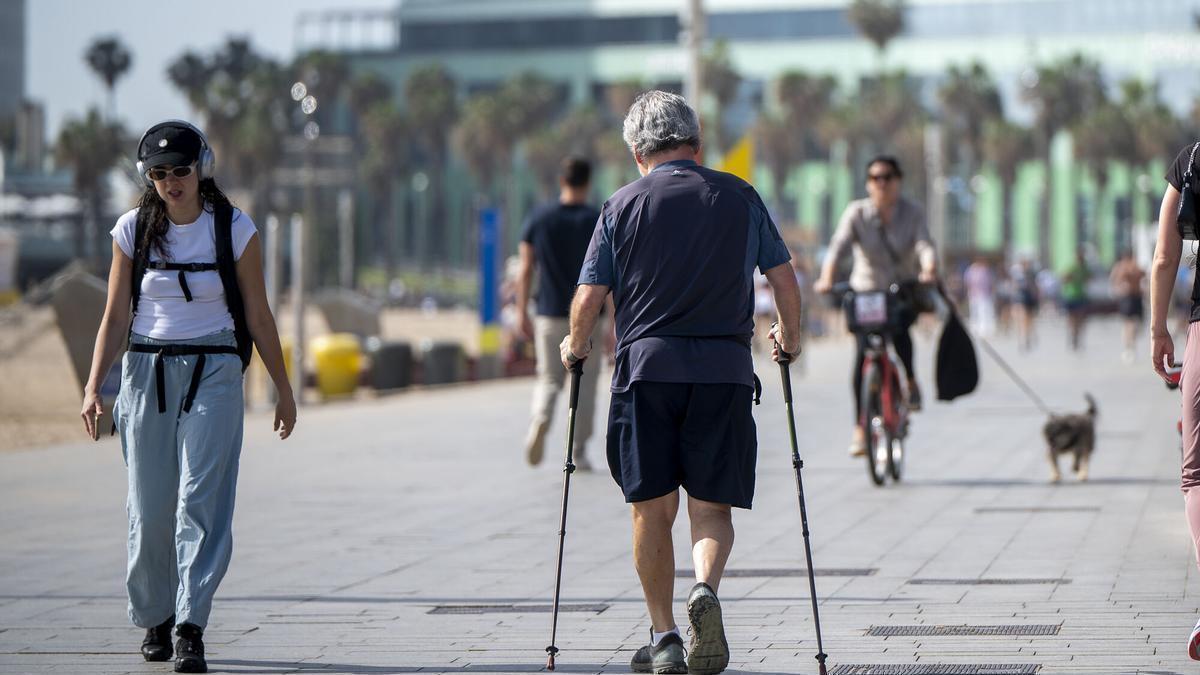 Un hombre que camina ayudado con bastones junto a la playa de la Barceloneta.