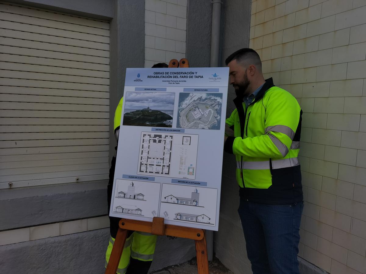 Dos técnicos sostienen  el panel con los planos de la futura residencia de artistas del faro de Tapia.