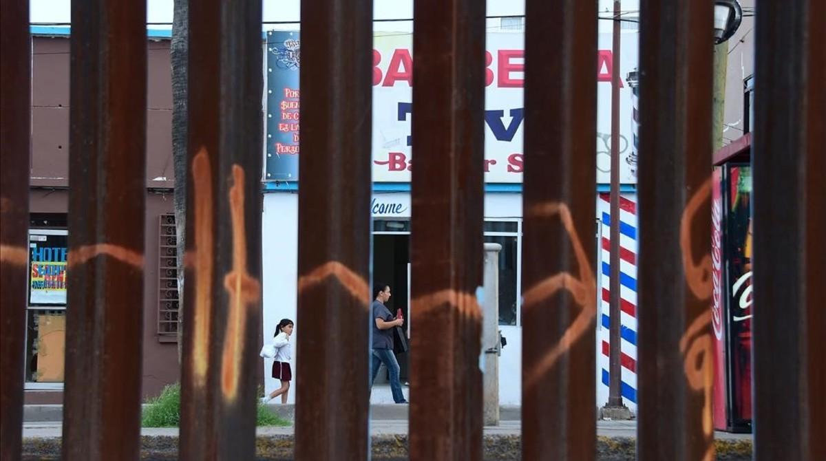 Una mujer y una niña pasan por delante de una barbería en Nogales, en el estado de Sonora (México), vistos a través de la valla fronteriza desde Nogales (Arizona), el 12 de octubre del 2016.