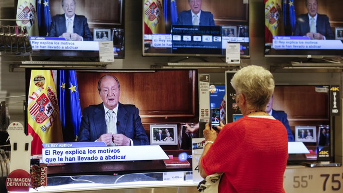 Una mujer graba con su móvil la comparecencia del Rey, ante una tienda de televisores en una calle de Valencia.