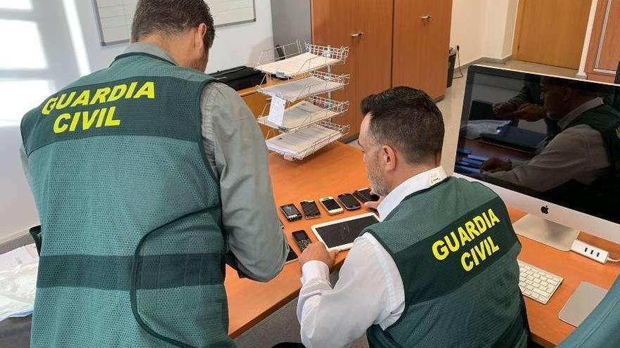 Dos agentes, con teléfonos y otros dispositivos incautados durante la operación. // Guardia Civil