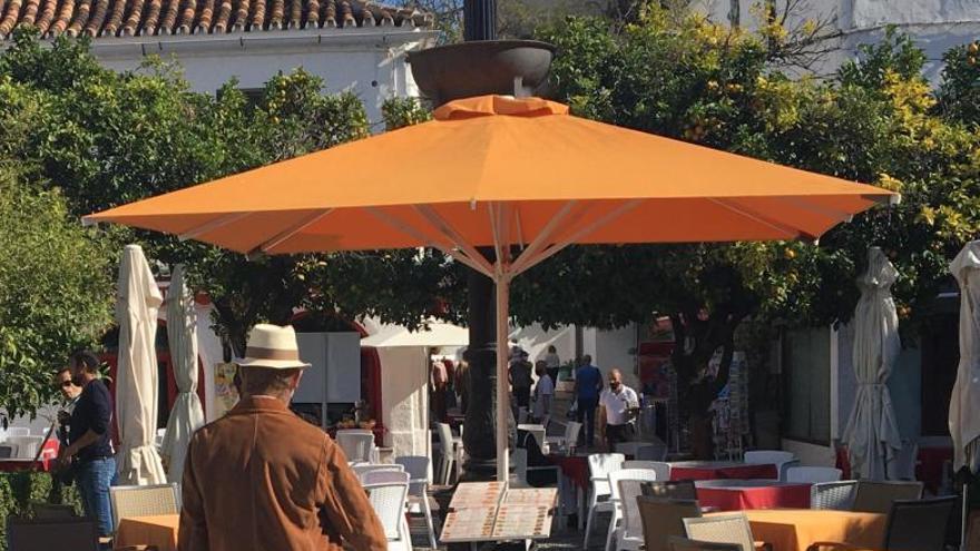 Un hombre pasa entre las mesas de restaurantes ubicados en la Plaza de Los Naranjos.