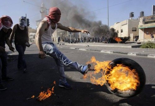 Palestinos dan patadas a un neumático después de prenderle fuego durante los enfrentamientos con la policía israelí en Shuafat, un barrio árabe de Jerusalén.