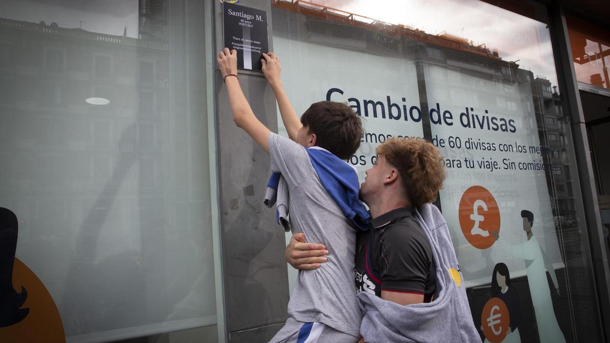 Dos estudiantes de la escuela Guinardó colocan un cartel de recuerdo a una persona sin techo fallecida en Barcelona.