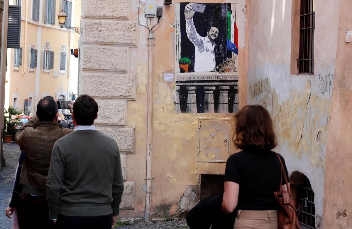 La gente pasa junto a un mural que representa al viceprimer ministro italiano Matteo Salvini tomando un selfie en el balcón de Benito Mussolini, cerca de la sede del ex dictador fascista días antes de una votación en las elecciones de la UE en Roma, Italia.