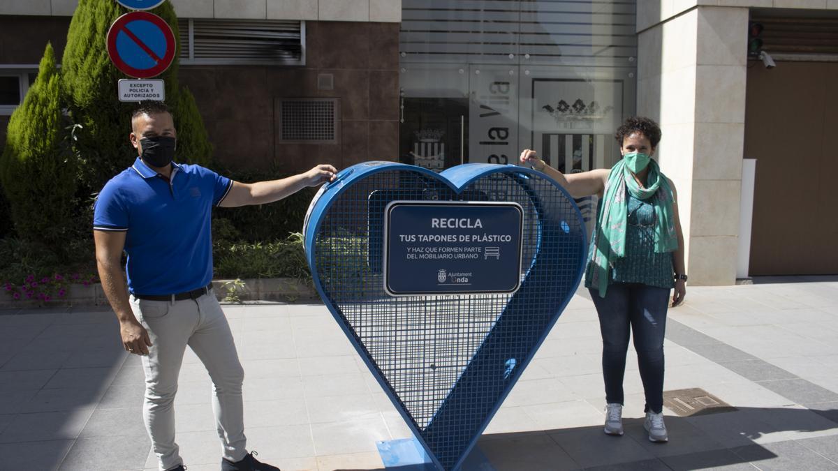 Carmina Ballester y Paco Pastor, con uno de los corazones metálicos para reciclar los tapones de plástico.